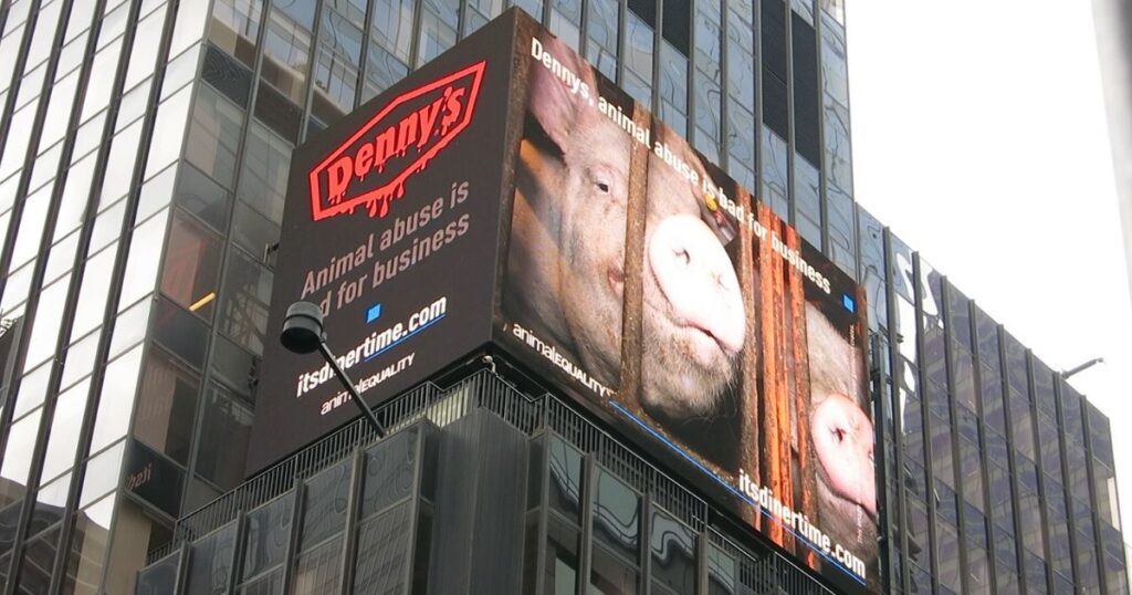 A digital billboard featuring a pig peering through the bars of a crate. The text reads, "Denny's animal abuse is bad for business."
