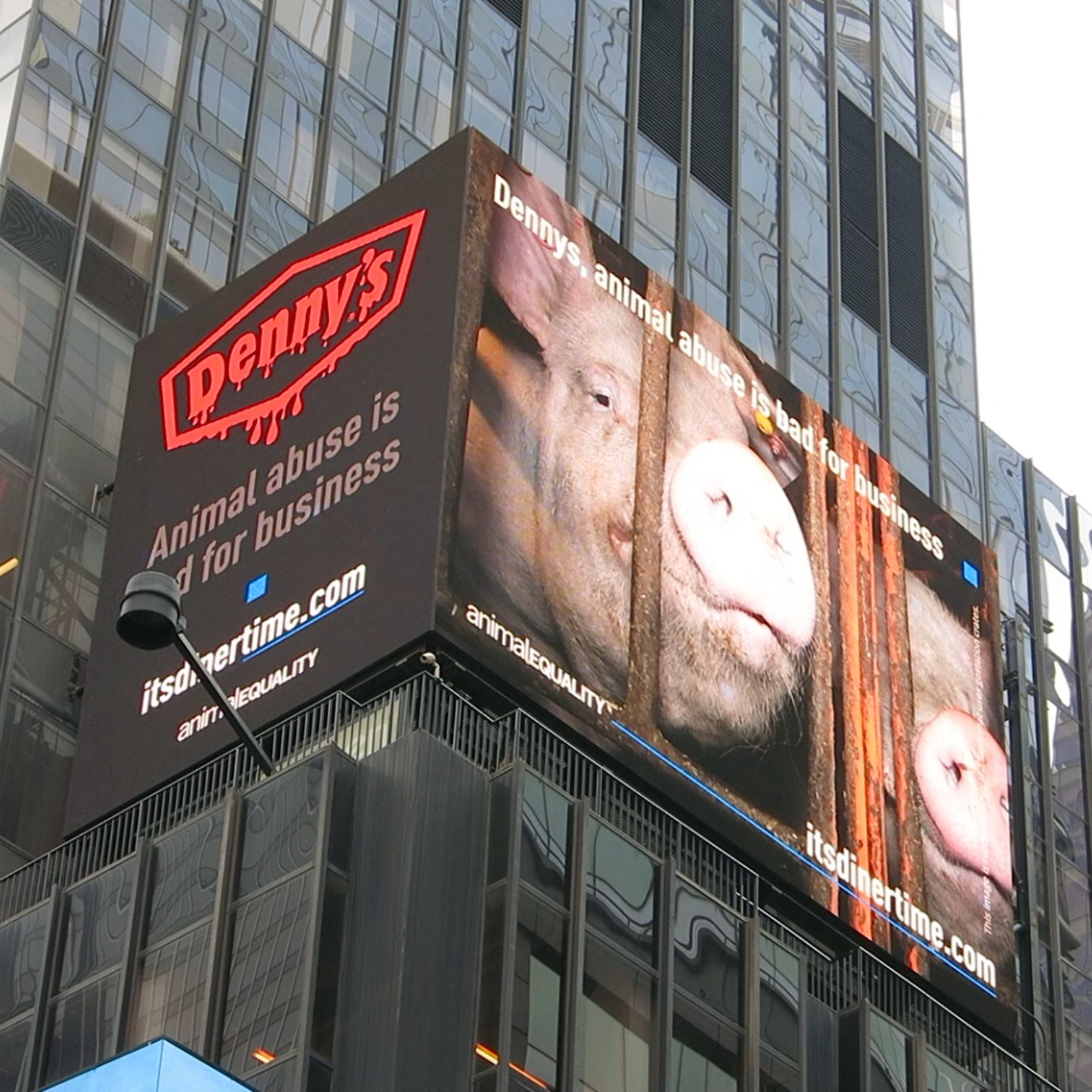 A digital billboard featuring a pig peering through the bars of a crate. The text reads, "Denny's animal abuse is bad for business."