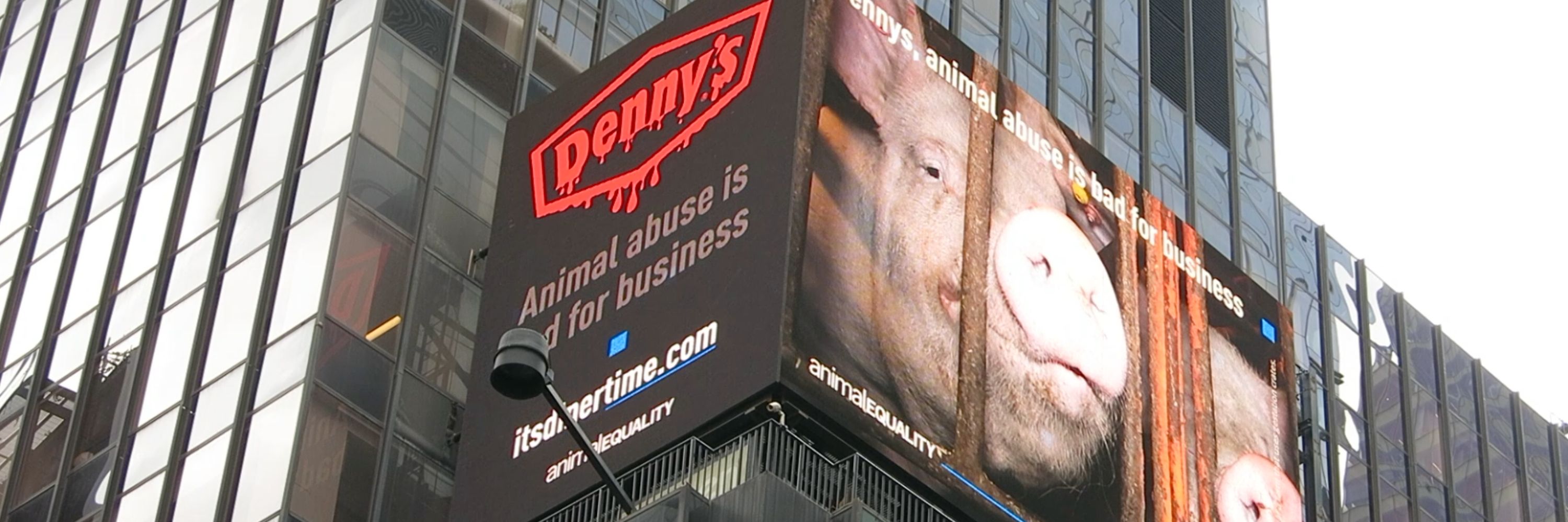 A digital billboard featuring a pig peering through the bars of a crate. The text reads, "Denny's animal abuse is bad for business."