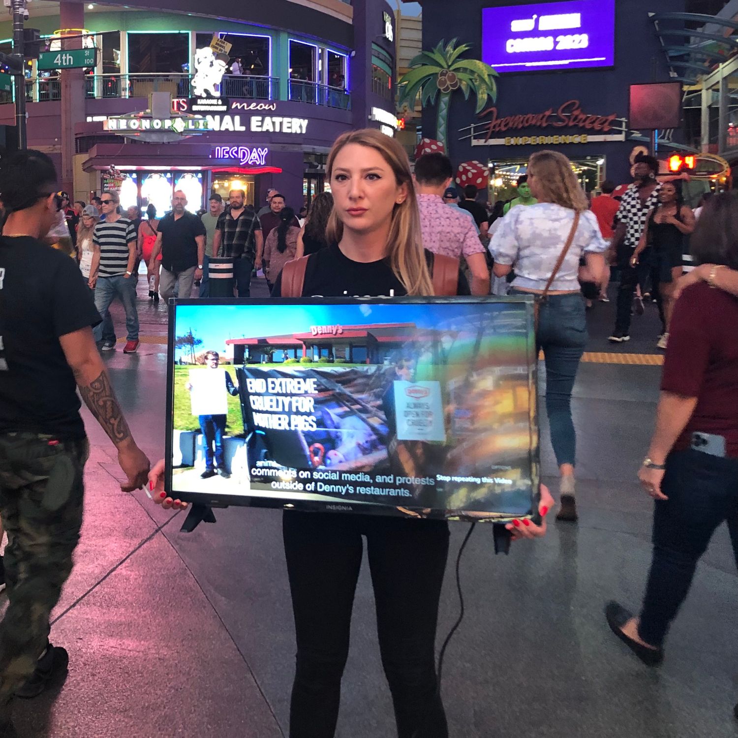 protestor standing holding a television that is playing a video of pigs in a cage