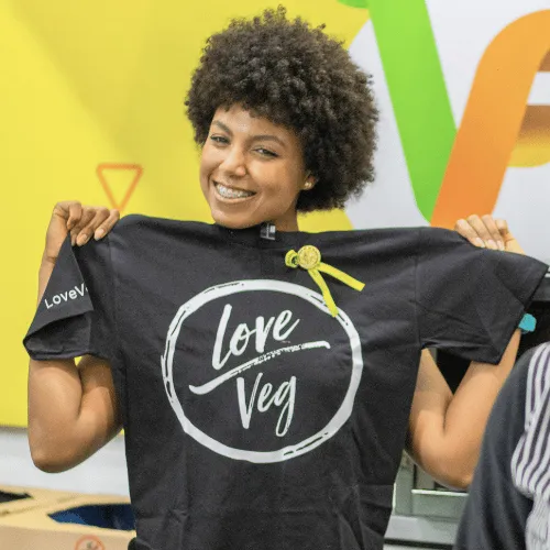 A woman holds up a black Love Veg t-shirt toward the camera.