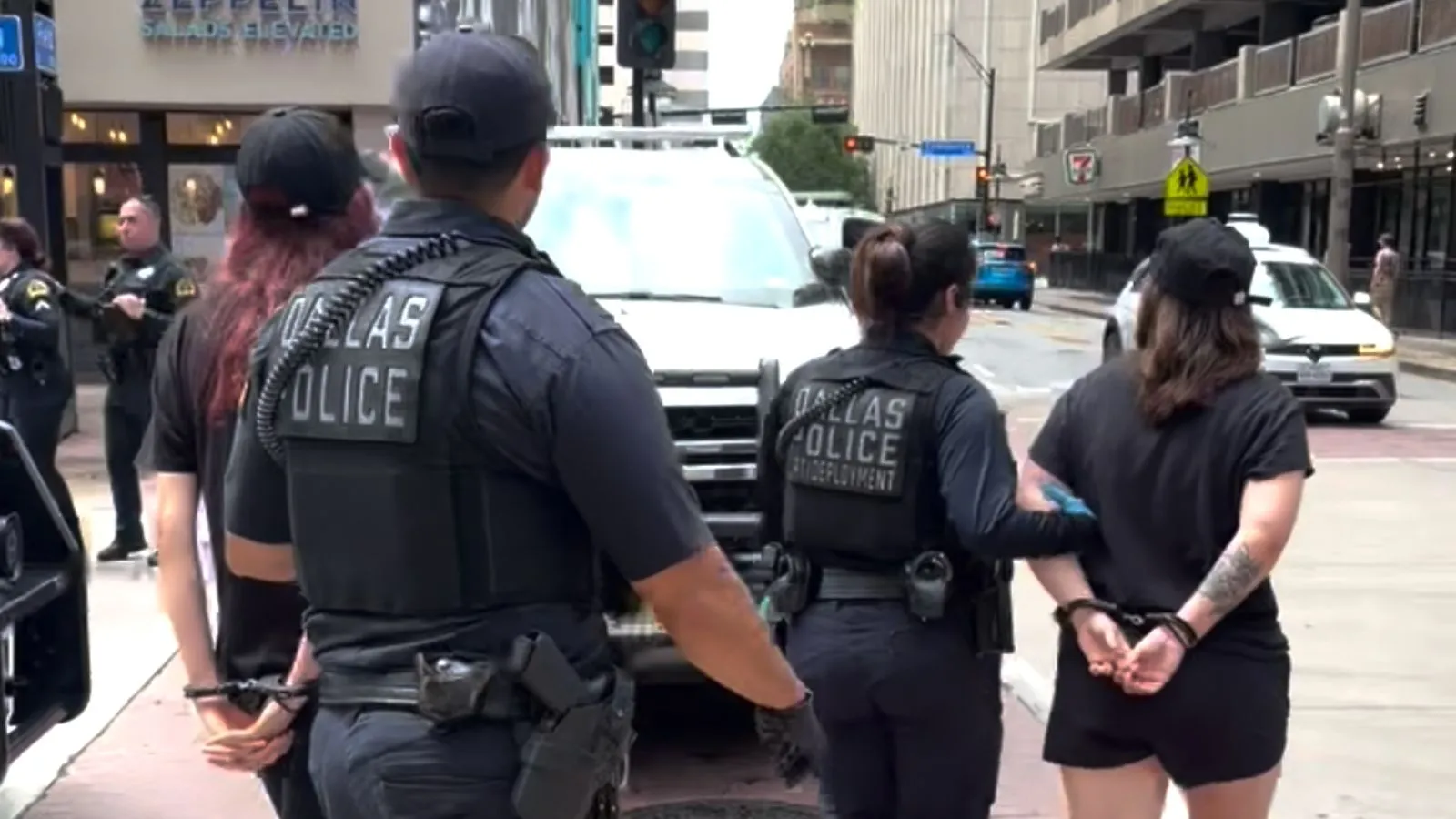 Two activists in handcuffs are being led to a police car, outside of a Marriott hotel in Dallas, Texas